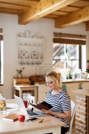 Older woman working from homeoffice. The retiree earning extra money during retirement. Woman paying bills online