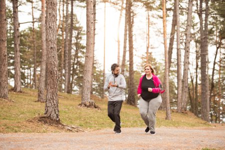 Eine übergewichtige Frau, die mit einem Freund in der Natur läuft. Bewegung im Freien für Menschen mit Fettleibigkeit, Unterstützung durch Freunde oder Fitnesstrainer.