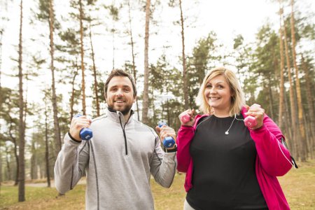 An overweight woman exercising outdoors with friend, fitness coach. Holding dumbbells