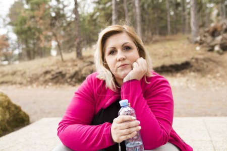 Foto de Overweight woman drinking water after run in nature. Exercising outdoors for people with obesity - Imagen libre de derechos