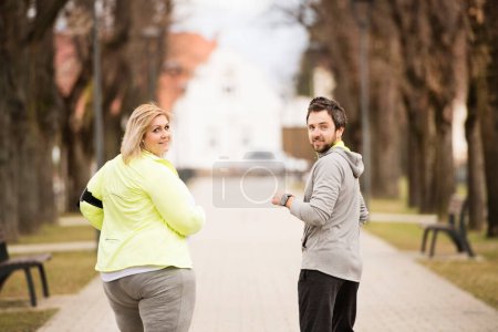Foto de Una mujer con sobrepeso corriendo en la naturaleza con un amigo. Ejercicio al aire libre para personas con obesidad, apoyo de un amigo o entrenador de fitness. - Imagen libre de derechos