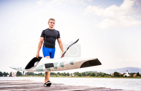 Young canoeist carry canoe and paddle, going into water, walking on wooden dock. Concept of canoeing as dynamic and adventurous sport.