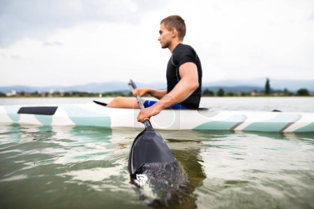 Canoéiste assis en canot tenant la pagaie, dans l'eau. Concept de canoë-kayak comme sport dynamique et aventureux. Vue arrière, sportif regardant la surface de l'eau, pagayant.