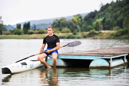 Young canoeist sitting on wooden dock. Concept of canoeing as dynamic and adventurous sport