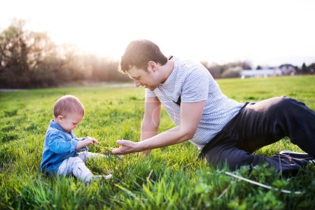 Téléchargez les photos : Père jouant avec le petit garçon tout-petit dans l'herbe, s'amusant pendant la chaude journée de printemps. Concept de fête des pères - en image libre de droit