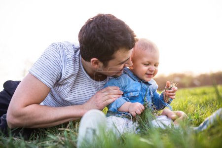 Téléchargez les photos : Père jouant avec le petit garçon tout-petit dans l'herbe, s'amusant pendant la chaude journée de printemps. Concept de fête des pères - en image libre de droit