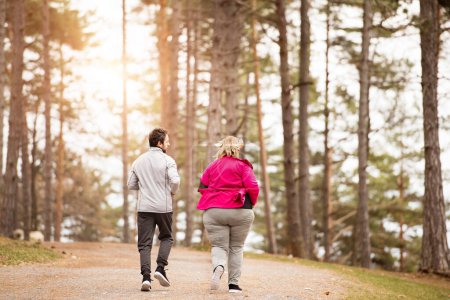 An overweight woman running in nature with friend. Exercising outdoors for people with obesity, support from friend or fitness coach. Rear view.