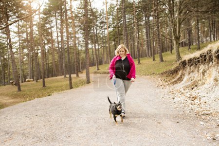 Übergewichtige Frau läuft mit Hund in der Natur. Bewegung im Freien für fettleibige Menschen
