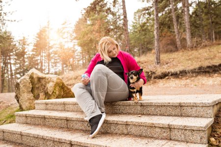 Overweight woman running with dog in nature, resting after workout. Exercising outdoors for people with obesity