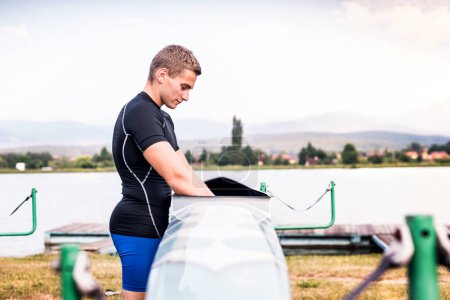 Junger Kanufahrer kümmert sich um sein Kanu und sein Paddel, putzt, trocknet. Konzept des Kanusports als dynamischer, abenteuerlicher Sport.
