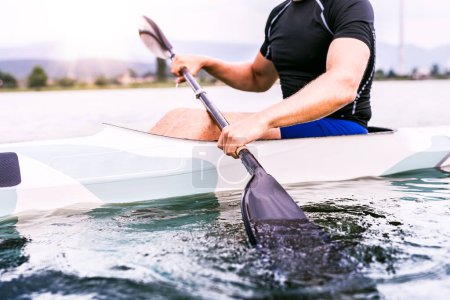 Canoeist man sitting in canoe holding paddle, in water. Concept of canoeing as dynamic and adventurous sport. Rear view, sportman looking at water surface, paddling.