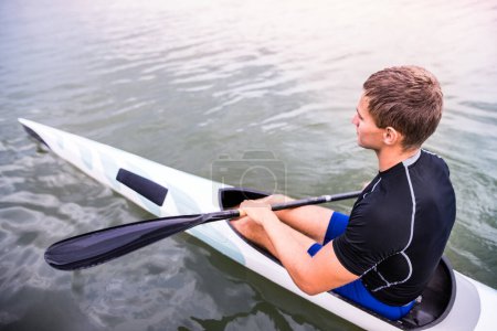 Téléchargez les photos : Canoéiste assis en canot tenant la pagaie, dans l'eau. Concept de canoë-kayak comme sport dynamique et aventureux. Vue arrière, sportif regardant la surface de l'eau, pagayant. - en image libre de droit