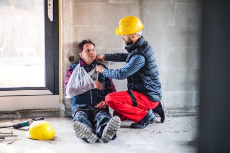 Foto de Colega que da primeros auxilios al trabajador lesionado después de un accidente en el sitio de construcción Concepto de seguridad y salud en el lugar de trabajo. - Imagen libre de derechos