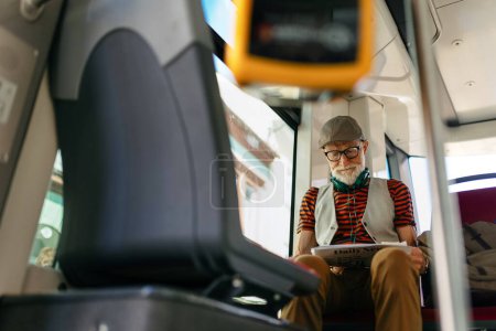 Älterer Mann, der mit dem Bus durch die Stadt fährt und eine Zeitung liest. Senior-Pendler fährt mit Straßenbahn zum Lebensmittelgeschäft und nutzt öffentliche Verkehrsmittel.