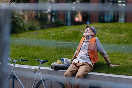 Stilvoller Senior sitzt im Stadtpark und genießt das warme Wetter. Pendler fahren Fahrrad