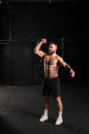 Photo for Man lifting a weight with hand, one arm dumbbell snatch, wearing only shorts, bare chest. Routine workout for physical and mental health. - Royalty Free Image