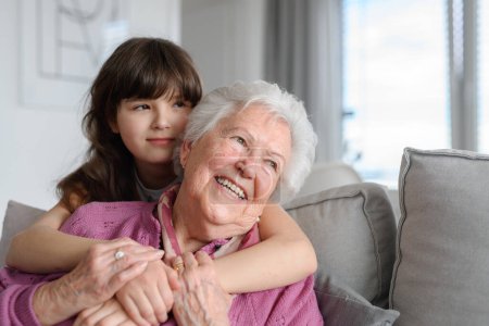 Foto de Linda chica abrazando gradmother por detrás, sonriendo. Retrato de una anciana que pasa tiempo con su nieta. - Imagen libre de derechos