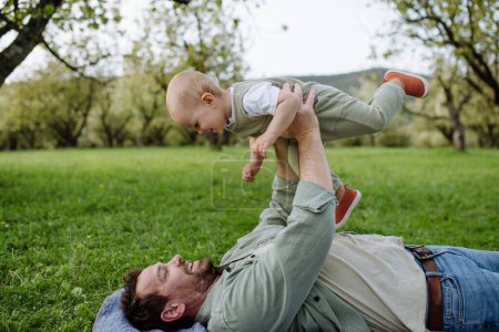 Foto de Un padre sosteniendo un bebé pequeño, jugando, divirtiéndose durante el cálido día de primavera. Concepto del día de los padres. - Imagen libre de derechos