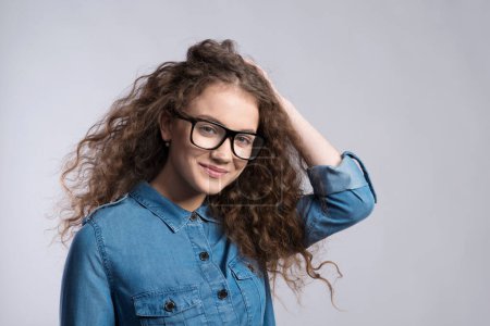 Téléchargez les photos : Portrait d'une magnifique adolescente aux cheveux bouclés et aux lunettes. Plan studio, fond blanc avec espace de copie. - en image libre de droit