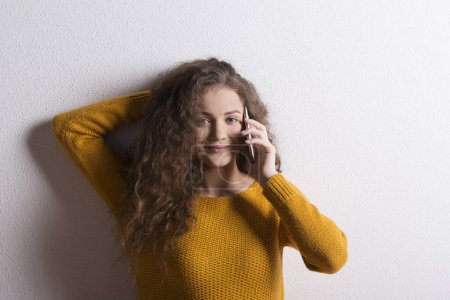 Foto de Retrato de una hermosa adolescente con el pelo rizado, haciendo una llamada telefónica. Captura de estudio, fondo blanco con espacio de copia. - Imagen libre de derechos