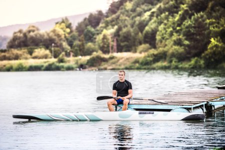 Photo for Canoeist man sitting in canoe paddling, in water. Concept of canoeing as dynamic and adventurous sport. Rear view, sportman looking at water surface, paddling. - Royalty Free Image