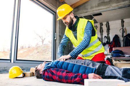 Colleague performing CPR on an injured worker lying on ground after accident. Concept of occupational safety and health in workplace.