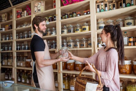 Photo for Handsome shop assistant serving customer in package-free store using reusable containers. Zero waste shops offering package-free bulk goods and sustainable alternatives - Royalty Free Image