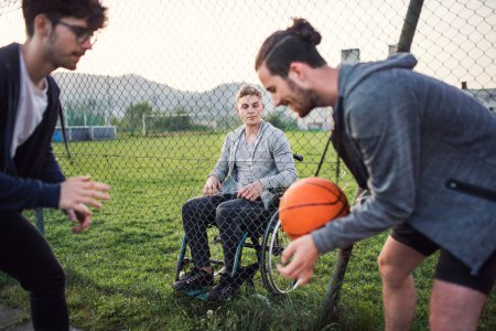 Behinderter junger Mann fühlt sich ausgeschlossen, möchte mit seinen Freunden Basketball spielen, aber wegen des Rollstuhls kann er nicht spielen.
