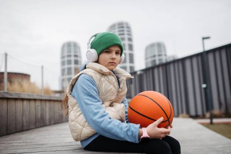 Triste chica sola en la ciudad, quiere jugar baloncesto. Jovencita pasando tiempo libre sola en la ciudad, sin amigos, sin actividad. Problemas de salud mental.
