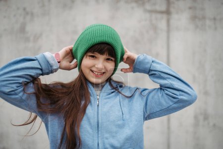 Portrait extérieur de mignonne jeune fille avec bonnet chapeau, riant. Fille aux cheveux longs debout sur une aire de jeux dans la ville.