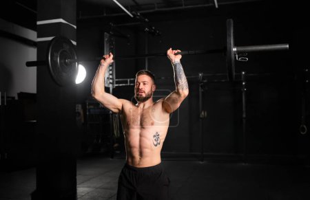 Photo for Strong man performing overhead squat, pressing barbell up, front body length shot. Routine workout for physical and mental health. - Royalty Free Image