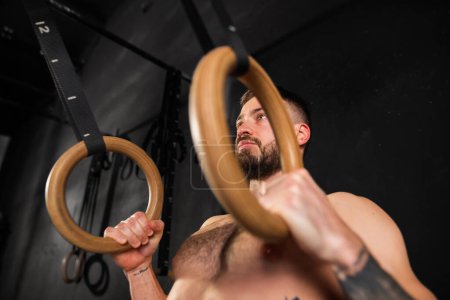 Téléchargez les photos : Homme fort debout près des anneaux dans la salle de gym, se préparant pour l'exercice. Entraînement quotidien de routine pour la force et la santé mentale. - en image libre de droit