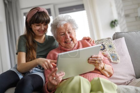 Grandmother with cute girl scrolling on tablet, girl teaching senior woman to work with technology, internet. Portrait of an elderly woman spending time with granddaughter.