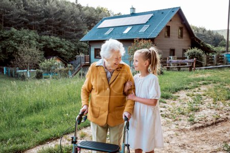 Foto de Nieta pasar tiempo con la abuela anciana, compañerismo. Señora mayor con andador a pie con chica joven. - Imagen libre de derechos