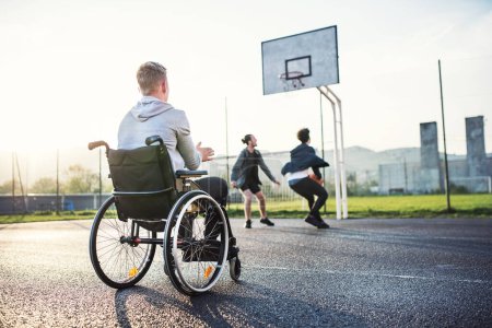 Behinderter junger Mann fühlt sich ausgeschlossen, möchte mit seinen Freunden Basketball spielen, aber wegen des Rollstuhls kann er nicht spielen.
