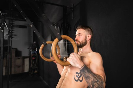 Hombre fuerte de pie junto a los anillos en el gimnasio, preparándose para el ejercicio. Ejercicio diario de rutina para la fuerza y la salud mental.