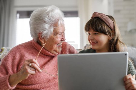 Téléchargez les photos : Grand-mère avec fille mignonne défilant sur tablette, fille enseignant aux femmes âgées à travailler avec la technologie, Internet. Portrait d'une femme âgée passant du temps avec sa petite-fille. - en image libre de droit