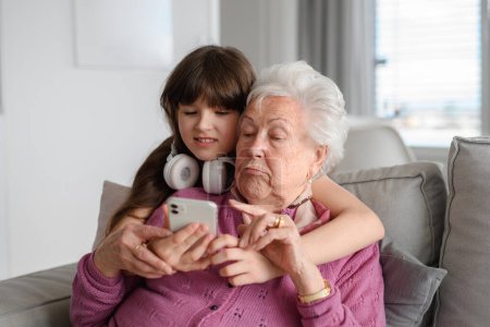 Abuela con linda chica desplazándose en el teléfono inteligente, chica enseñando a las mujeres mayores a trabajar con la tecnología, Internet. Retrato de una anciana que pasa tiempo con su nieta.