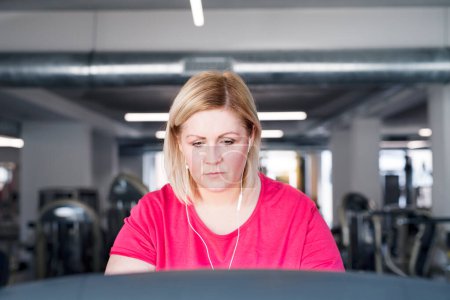 Overweight woman exercising on treadmill machine in gym.