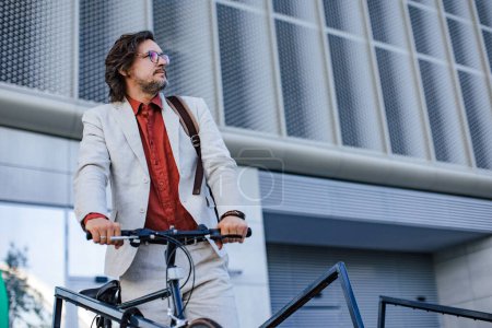 Portrait d'un homme d'affaires mature debout à vélo, se déplaçant du bureau à vélo, rentrant chez lui. bel homme avec des lunettes, sac à dos en costume.