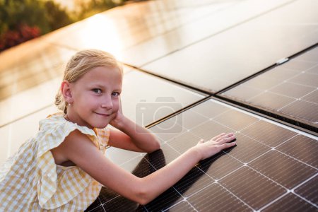 Girl lying on roof with solar panels during sunset, smiling. Sustainable future for next generation concept.
