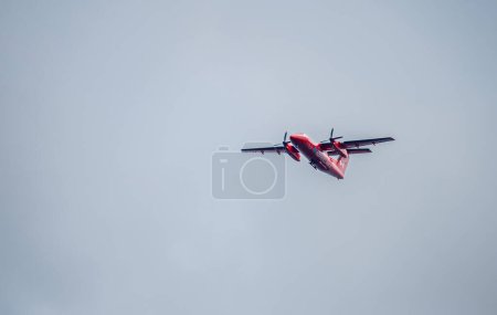 Photo for A red Transport Canada aerial Dash-8 turboprop NASP surveillance plane flys overhead near on an overcast day. - Royalty Free Image