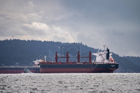 Téléchargez les photos : Le vraquier Ultramax Belisland et un autre cargo sont ancrés près de Gabriola Island, le navire militaire Stikine navigue entre eux. - en image libre de droit