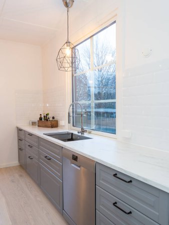 Téléchargez les photos : Intérieur de la cuisine moderne armoire grise évier carrelage blanc par la fenêtre - en image libre de droit
