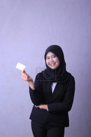 A woman wearing a hijab and holding a white business card.