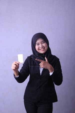 A woman in a black suit is holding a white business card and smiling.