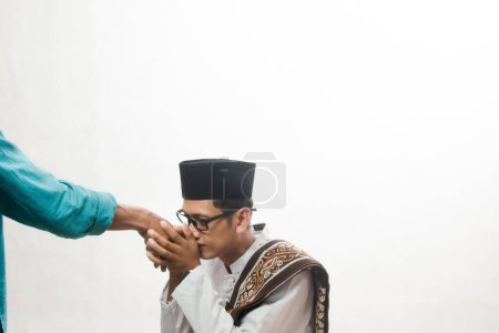 Foto de Hombre musulmán asiático en camisa blanca con piel marrón con camisa koko estrechando la mano con sus padres sobre fondo blanco estudio, concepto tradicional sungkem indonesio - Imagen libre de derechos