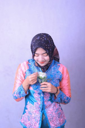 closeup of Asian Indonesian hijab woman holding flowers happily, smiling looking down protected on white background