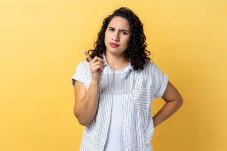 Photo for Portrait of serious strict woman with dark wavy hair pointing finger at camera and looking with dissatisfied suspicious expression. Indoor studio shot isolated on yellow background. - Royalty Free Image