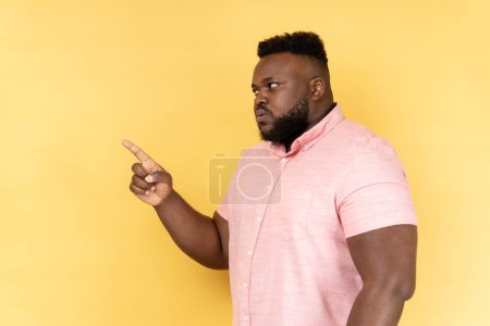 Photo for I told you. Side view of man wearing pink shirt pointing finger and looking ahead with dissatisfied suspicious expression, warning about troubles. Indoor studio shot isolated on yellow background. - Royalty Free Image